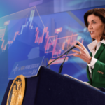 A governadora de Nova York, Kathy Hochul, fala no pódio enquanto o gráfico do mercado de ações ilustra a ordem executiva que proíbe o uso de informações privilegiadas nos mercados de previsão.