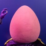 Dois chocolateiros vestindo uniformes roxos pintando o maior Cadbury Mini Egg do mundo.