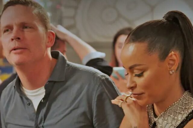 Homem falando enquanto uma mulher olha para baixo com as mãos entrelaçadas.