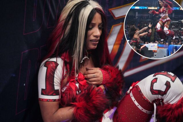 Mercedes Mone está em um ringue de luta livre, vestindo uma roupa vermelha e branca com braçadeiras felpudas e um cinto de campeonato na cintura.