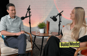 O que os fundadores podem aprender com as demissões e a recuperação de Anjuna A podcast-style interview setup shows a man and a woman seated across from each other in armchairs, speaking into microphones. They sit beside a small round table with water glasses, books, and a potted plant, against a white brick wall backdrop. A “TechCrunch Build Mode” logo appears in the lower corner.