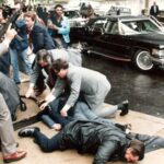 Um assessor de imprensa ferido e um membro do Serviço Secreto estão caídos no local da tentativa de assassinato do presidente Ronald Reagan em 1981.