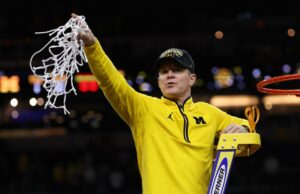 O técnico do Michigan, Dusty May, assinou extensão após ganhar o título nacional O técnico Dusty May, do Michigan Wolverines, segura a rede após derrotar o UConn Huskies.
