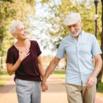 Um casal mais velho sorridente, de mãos dadas, andando em um parque.