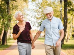 O traço de personalidade que reduz o risco de demência: estudo Um casal mais velho sorridente, de mãos dadas, andando em um parque.