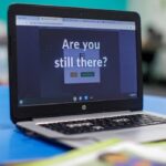 Retrato de uma mulher sorridente com longos cabelos escuros, óculos e usando um lenço escuro sobre um suéter rosa.