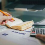 Planos ilimitados legados da AT&T enfrentam aumentos de preços e são uma bagunça | Foto mostra um homem com calculadora, notebook e MacBook com gráficos sobre a mesa