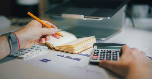 Planos ilimitados legados da AT&T enfrentam aumentos de preços e são uma bagunça | Foto mostra um homem com calculadora, notebook e MacBook com gráficos sobre a mesa