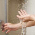 As mãos de uma pessoa pegando água de um chuveiro.