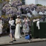Turistas asiáticos tiram fotos em frente a glicínias em flor em frente a uma casa no oeste de Londres