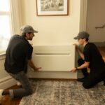 Two men install a heat pump on a wall.