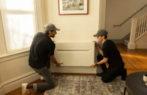 Por que um ex-engenheiro de AirPods está agora construindo bombas de calor Two men install a heat pump on a wall.