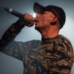 Capital Bra se apresentando ao vivo no palco com microfone durante show em meio à polêmica sobre multa do regulador de jogos de azar da Alemanha. Regulador alemão visa Capital Bra por suposto caso de promoção ilegal de jogos de azar