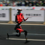 The fastest humanoid robot, an H1made by Honor, runs beside human runners at the start on its way to winning the Beijing Humanoid Half Marathon.