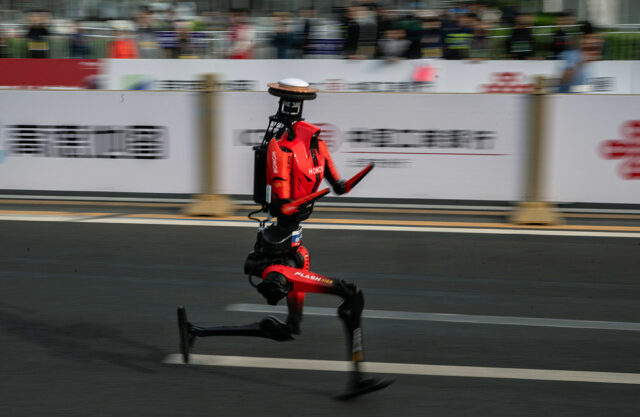 The fastest humanoid robot, an H1made by Honor, runs beside human runners at the start on its way to winning the Beijing Humanoid Half Marathon.