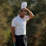 Scottie Scheffler tira o boné branco, segurando-o logo acima da cabeça, e parece frustrado no buraco 18 do Masters.