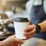 Barista entregando uma xícara de café para viagem a um cliente.