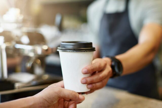 Barista entregando uma xícara de café para viagem a um cliente.