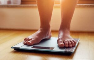 Sou um médico especialista em obesidade – por que sua perda de peso pode estagnar, mesmo quando sua dieta não mudou Pés descalços de uma mulher em pé sobre uma balança.