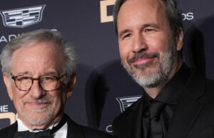 Steven Spielberg elogia os filmes ‘Duna’ de Denis Villeneuve como alguns de seus filmes de ficção científica favoritos: ‘Tal fã’ Um homem mais velho, de cabelos grisalhos e barba, fala ao microfone, vestindo um paletó esporte, diante de um fundo cinza suave.