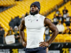 Texans entregam contrato histórico de US$ 150 milhões a Will Anderson Um jogador de futebol americano vestindo um gorro e uma camisa sem mangas com o logotipo da NFL, com as mãos na cintura, em pé no campo com assentos amarelos ao fundo.