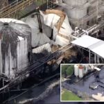 Uma instalação industrial mostra um tanque de asfalto rompido, vazando asfalto preto no chão, e dois tanques intactos com asfalto escuro escorrendo pelas laterais.