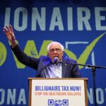 O senador Bernie Sanders fala em um pódio em frente a uma faixa azul que diz