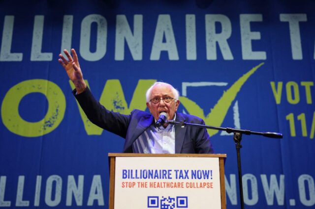 O senador Bernie Sanders fala em um pódio em frente a uma faixa azul que diz 