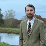 Um jovem deitado em uma cama de hospital faz sinal de positivo.