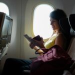 A plane passenger reading a note in her seat by a window.
