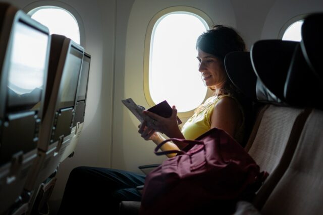 A plane passenger reading a note in her seat by a window.