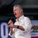 O governador da Califórnia, Gavin Newsom, falando ao microfone com a boca aberta.