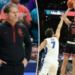 Um jogador de basquete com uniforme preto e vermelho atirando um arremesso sobre um jogador adversário.