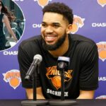 Karl-Anthony Towns sorrindo em uma coletiva de imprensa com dois microfones à sua frente.
