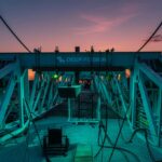 A drilling rig stands in front of a sunset.