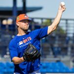 Um jogador de beisebol com uma camisa azul do Mets e um chapéu laranja jogando uma bola de beisebol durante o treinamento de primavera.