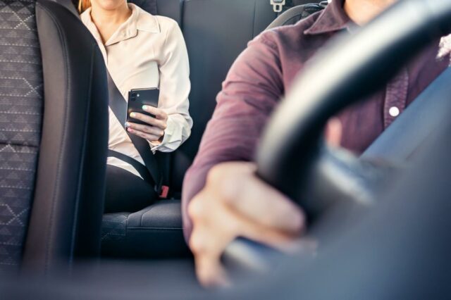 imagem de uma pessoa ao telefone no banco de trás com um motorista ao volante