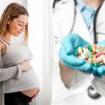 Uma mulher grávida com blusa e cardigã cinza, tocando suavemente a barriga enquanto está perto de uma janela, sorrindo para a barriga.