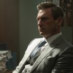 A man in a grey suit sitting down and looking sad