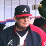 Bobby Cox com uniforme do Braves, segurando uma xícara e papéis no banco de reservas.