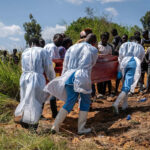 Glody Murhabazi/AFP via Getty Images - FOTO: Profissionais de saúde carregam o caixão no cemitério para o enterro de uma pessoa suspeita de ter morrido de Ebola em Bunia, no leste da República Democrática do Congo, em 25 de maio de 2026.