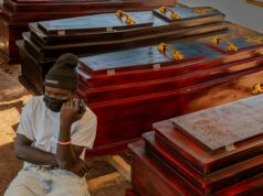‘Cada hora fazendo caixões’: Funerais, velórios proibidos enquanto a OMS eleva a ameaça do Ebola para ‘muito alto’ Christian Djakisa, 18 anos, vende caixões na sua loja em Bunia, na República Democrática do Congo.