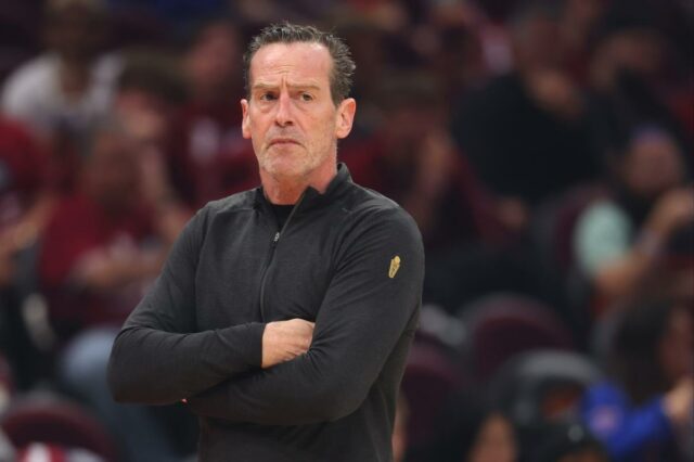 Cavaliers tomam decisão de Kenny Atkinson após serem varridos pelos Um homem com uma camisa preta de mangas compridas com um emblema dourado no ombro esquerdo, braços cruzados, olhando atentamente.