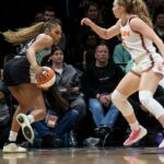 Betnijah Laney-Hamilton dribla a bola de basquete enquanto é defendida por Gianna Kneepkens durante um jogo.