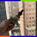Colagem de um frasco de soro facial multivitamínico Truskin e a mão de uma pessoa com um pouco de soro.