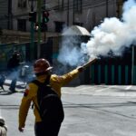 As chamas sobem de uma caixa de papelão enquanto mineiros entram em confronto com a tropa de choque durante um protesto exigindo a renúncia do presidente boliviano Rodrigo Paz, em La Paz, em 18 de maio de 2026.