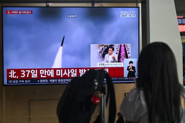 A woman watches a television screen showing a news broadcast with file footage of a North Korean missile test, at a train station in Seoul on May 26, 2026.