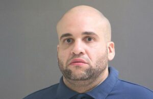 Crescimento criminoso na carreira com 166 prisões, 55 condenações desde 1999, condenado à prisão perpétua Mugshot de um homem careca com barba vestindo uma camisa pólo azul.