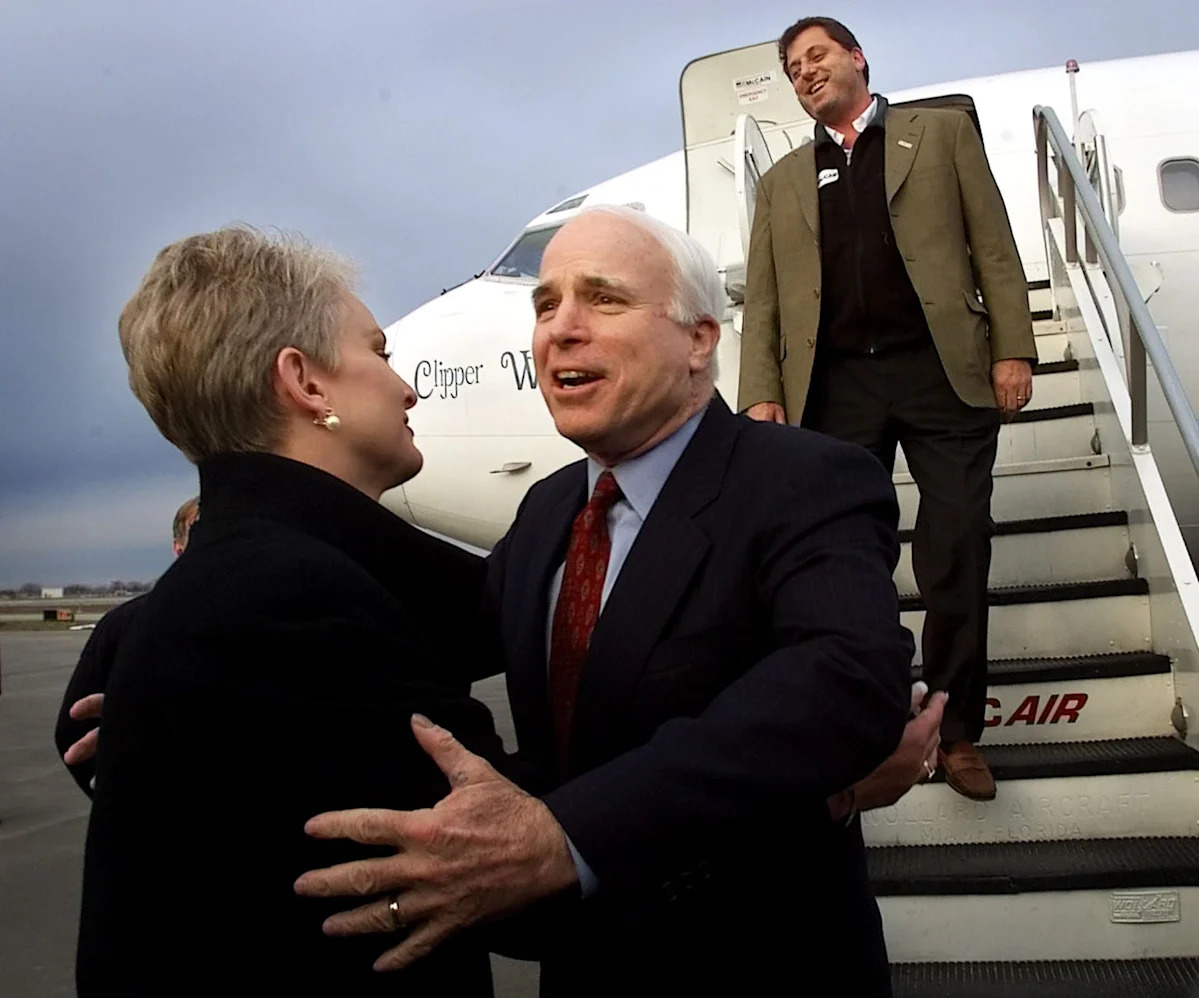 Sonhar. John McCain estende a mão para sua esposa Cindy, acompanhado pelo filho, Doug McCain, quando o então candidato presidencial republicano chega a Syracuse, Nova York, em 4 de março de 2000.