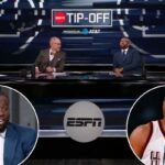 Draymond Green falando em um evento, vestindo um terno azul e uma camisa branca com microfone acoplado.